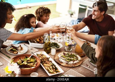 Familie, Essen und Anfeuern zum Mittagessen, Feiern und Entspannen im Hinterhof bei einem Glas Wein am Tisch. Eltern, Kinder und Gruppe von Menschen im Freien vorbei Stockfoto