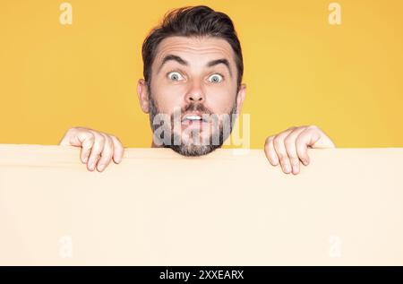 Erstaunter Kerl mit leerer Werbebanner isoliert im Studiohintergrund. Porträt eines überraschten Mannes mit leerem Plakat. Erstaunter Mann, der ein leeres Poster zeigt Stockfoto