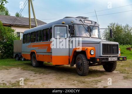 Ein Vintage-Bus aus sowjetischer Zeit mit orangefarbener und grauer Farbe, der in einer ländlichen Gegend in der Nähe eines Hauses geparkt ist und ein Gefühl von Nostalgie und historischem Transport weckt. Stockfoto