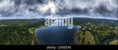 Sonnenstrahlen brechen durch Sturmwolken über dem See Grönsjön, Camper und Boote säumen das Ufer bei einem Campingplatz, dem Naturschutzgebiet Långfjället in Dalarna, Schweden. Stockfoto