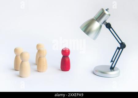 Tischlampe mit Fokus auf rote Holzfigur, die Führungsrolle oder eine ausgewählte Person repräsentiert. Stockfoto