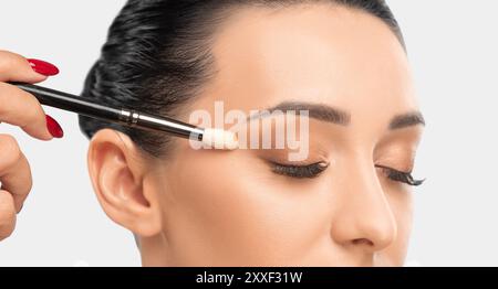 Porträt einer charmanten brünetten Frau mit gesunder, sauberer Haut. Make-up-Künstler wendet Lidschatten an. Das Konzept der ästhetischen Kosmetologie und Make-up. Stockfoto