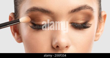 Porträt einer charmanten brünetten Frau mit gesunder, sauberer Haut. Make-up-Künstler wendet Lidschatten an. Das Konzept der ästhetischen Kosmetologie und Make-up. Stockfoto