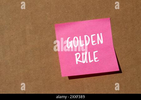 Goldene Regel-Nachricht auf rosa Papier mit Papphintergrund geschrieben. Konzeptionelles goldenes Regelsymbol. Kopierbereich. Stockfoto