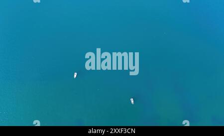 Zwei kleine Boote treiben mühelos auf ruhigem, leuchtend blauem Wasser, reflektieren die helle Mittagssonne und schaffen eine friedliche Atmosphäre in einem küstenparadies Stockfoto