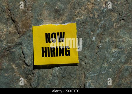 Jetzt ist die Einstellungsnachricht auf gerissenem gelbem Papierstück mit Steinhintergrund geschrieben. Symbol „Conceptual Now Hiring“. Kopierbereich. Stockfoto