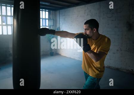 Der Kämpfer trifft in einem dunklen Fitnessstudio einen Boxsack. Stockfoto