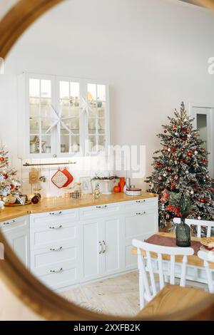 Gemütliche Weihnachtsküche im Spiegel mit einem mattierten Baum mit roten Ornamenten, weißen Schränken und festlicher Weihnachtsdekoration Stockfoto