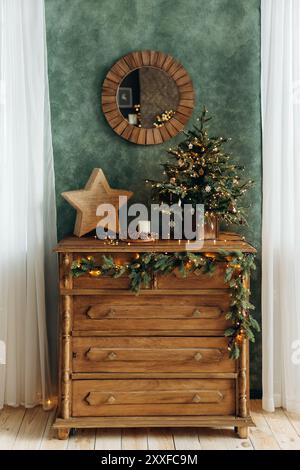 Vintage Holzkommode mit Weihnachtsdekor. Ein dekorativer Stern und ein kleiner grüner Weihnachtsbaum mit Blumenlampen auf einer Kommode Stockfoto