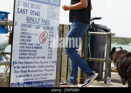 Preislistenschild und man and Dog gehen auf die Mudeford Spit Ferry, Mudeford Quay, Großbritannien Stockfoto