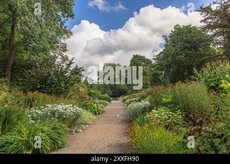 Schmaler Kiesweg durch den Park mit Blumenbeeten und Bäumen. Stockfoto