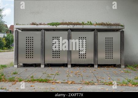 Ästhetischer Abfalleimer mit Metalltüren, Holz und Pflanzen vor einer Hauswand Stockfoto