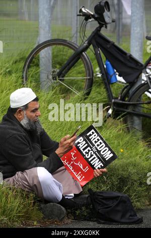 Blackburn, England, Großbritannien. August 2024. Ein Demonstrant sitzt am Rande und hält während der Demonstration vor den Haupttoren des BAE Systems ein Zeichen˜Freiheit für Palästina. Demonstranten beschuldigen BAE Systems, am Völkermord in Gaza beteiligt zu sein, indem sie Teile für die F-35-Kampfflugzeuge in ihrer Anlage in Samlesbury herstellen, die beim Luftangriff auf Gaza und den Jemen eingesetzt wurden. Seit dem 10/24 wurden über 5000 Luftangriffe auf Gaza gerichtet, bei denen Tausende von Zivilisten getötet wurden, darunter 16.500 Kinder. Quelle: ZUMA Press, Inc./Alamy Live News Stockfoto