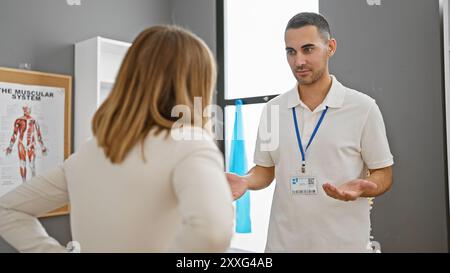 Ein Therapeut spricht mit einer Patientin in einer Reha-Klinik mit einem muskulären System im Hintergrund. Stockfoto