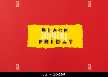 Black friday-Konzept. Draufsicht des gelben Papierbogens und des schwarzen freitagstexts auf rotem Hintergrund. Text im Rahmen. Komposition Black Friday. Lebendig Stockfoto