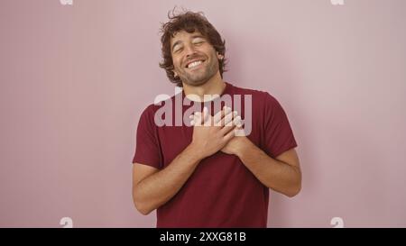 Lächelnder junger hispanischer Mann mit Händen am Herzen vor einem rosa isolierten Hintergrund. Stockfoto