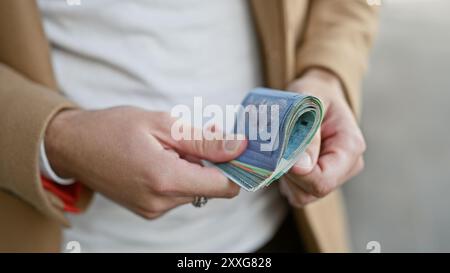 Nahaufnahme eines jungen hispanischen Mannes, der malaysisches Ringgit-Bargeld auf einer städtischen Straße hält Stockfoto