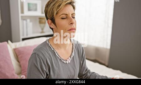 Eine hispanische Frau mit kurzen blonden Haaren sitzt ruhig in einem Schlafzimmer und ruft Ruhe und Komfort hervor. Stockfoto