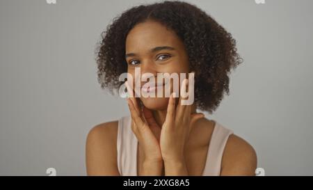 Eine schöne junge afroamerikanische Frau mit lockigen Haaren posiert vor einem isolierten weißen Hintergrund und zeigt ihre strahlende Haut und ihr selbstbewusstes Lächeln. Stockfoto