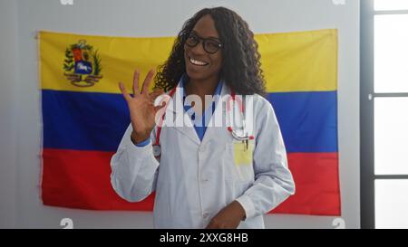 Eine afroamerikanische Ärztin mit lockigen Haaren macht eine gute Geste, die drinnen vor einer venezolanischen Flagge steht, in einem Wahlstudienzimmer Stockfoto