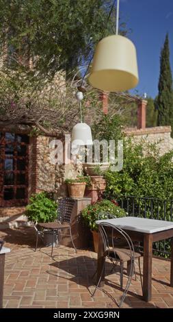 Eine gemütliche Terrasse mit Hängelampen, Topfpflanzen und Terrassenmöbeln lädt zum Entspannen in mediterraner Umgebung ein. Stockfoto