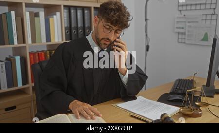 Junger Mann Richter im Amt mit Büchern und juristischen Waagen, der telefoniert, während er Rechtsdokumente überprüft Stockfoto