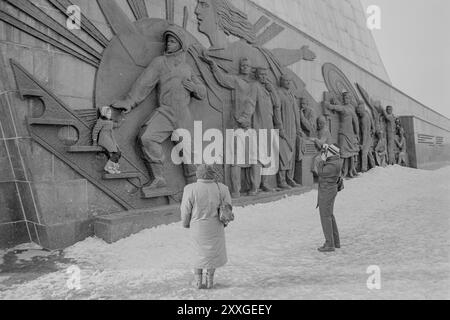 Ein Mann macht ein Foto von einem Kind am Fuß des Monuments für die Eroberer des Weltraums, während eine Frau zusieht. Das Denkmal in der Moskauer Ausstellung der Errungenschaften der Volkswirtschaft (VDNKh) wurde 1964 erbaut und trägt einen 350 Meter hohen Obelisken, der von einem Raumschiff gekrönt wird. Die Reliefs zeigen Männer und Frauen, die am sowjetischen Raumfahrtprogramm arbeiteten, darunter ein Kosmonaut, Wissenschaftler und Ingenieure. Stockfoto