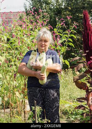 Proud Harvest: Vertikales Porträt einer älteren ukrainischen Frau mit frisch geerntetem Zucchini im Dorf Volyn Stockfoto