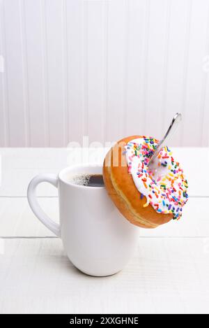 Nahaufnahme einer Tasse heißen Kaffees mit einem Donut, der vom Löffel in der Tasse hängt. Vertikal mit Kopierraum. Stockfoto