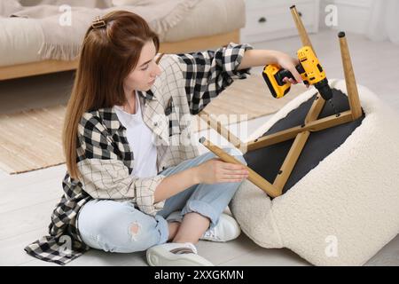 Frau mit elektrischem Schraubenzieher, der den Sessel zu Hause zusammenbaut Stockfoto