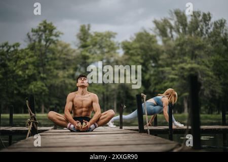 Mann und Frau üben Yoga auf hölzernem Dock in ruhiger Waldlage Stockfoto