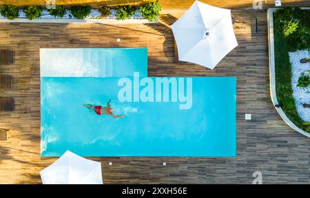 Aus der Vogelperspektive auf den Mann, der allein im exklusiven Villa Pool schwimmt. Konzept der Ruhe und Eleganz in einem privaten Rückzugsort Stockfoto