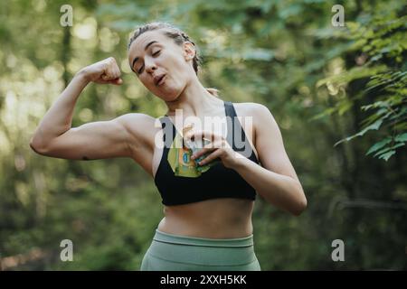 Sportliche Frau beugt Muskeln beim Essen einer Snackbar im Wald Stockfoto