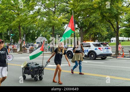 Washington DC, USA - 19.08.2024: Eine Gruppe von Menschen marschiert die Straße hinunter und hält eine palästinensische Flagge und ein Schild. Der Polizeiwagen ist hinter ihnen Stockfoto