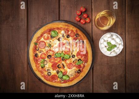 Pepperoni Pizza mit Wein, Tomaten, Mozzarella und Basilikum, geschossen von oben auf einem dunklen Hintergrund im Landhausstil mit einem Platz für Text Stockfoto