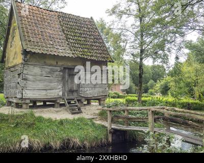 Alte Holzhütte mit moosbedecktem Dach am Ufer eines kleinen Baches, umgeben von dichter Vegetation, Bad Zwischenahn, ammerland, deutschland Stockfoto