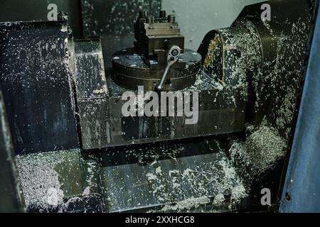 Nahaufnahme der CNC-Fräsmaschine, die Metallteile bearbeitet, mit angesammelten Metallspänen und Kühlmittelspritzern im Arbeitsbereich Stockfoto