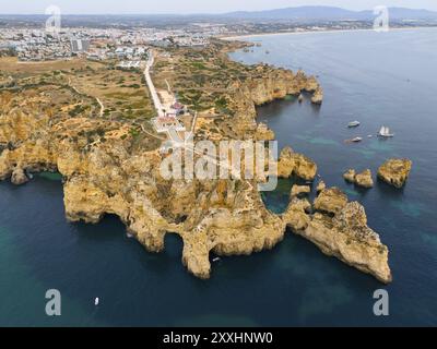 Steile Klippen und felsige Küste mit blauem Meer, jenseits einer Stadt und fernen Bergen, aus der Vogelperspektive, Ponta da Piedade, Point of Mercy, Lagos, Algarve, Po Stockfoto