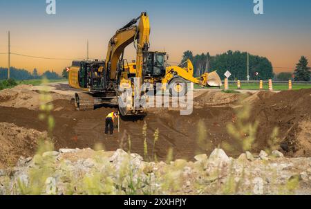 Bagger und Lader arbeiten bei Sonnenuntergang auf der Straße Stockfoto