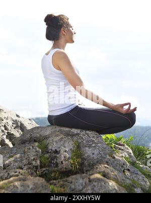 Attraktive junge Frau, die eine Yoga-Pose für Gleichgewicht auf hohen Felsen in den Bergen sonnigen Tag blauer Himmel mit Wolken zu tun Stockfoto