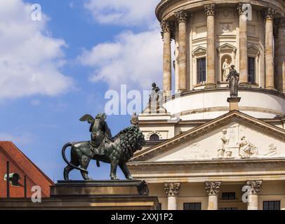 Statue eines Engels, der auf einem Löwen reitet und Harfe spielt, mit der französischen Kathedrale im Hintergrund Stockfoto