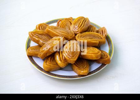 Köstliches gaja (auch bekannt als Khaja, Chiroti oder Chiroti) auf einem weißen Teller auf einer hellen Holzoberfläche. Dieses traditionelle süße Leckerli ist in Bangl beliebt Stockfoto