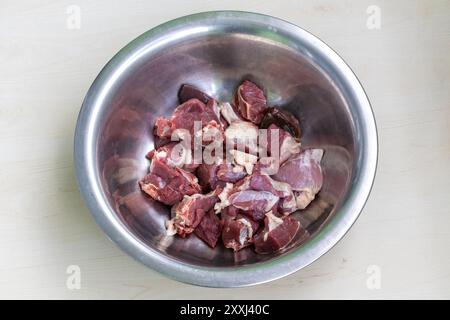 Frische rohe Hammelstücke in Stahlschale auf hellem Holzhintergrund. Bereit zum Kochen. Stockfoto