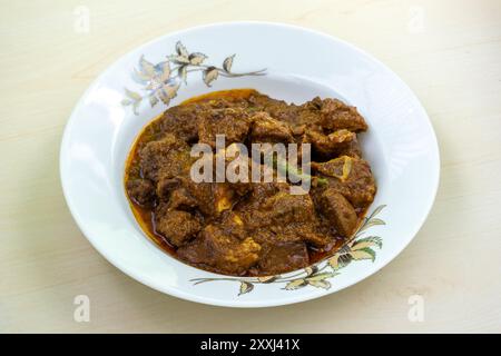 Köstliches Hammelcurry auf einer weißen Keramikplatte auf hölzernem Hintergrund. Hammelbhuna ist ein beliebtes, aromatisches und würziges Gericht in Bangladesch. Stockfoto