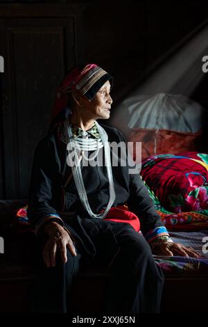 Ethnische Minderheit Tay Frau, die aus einem hell beleuchteten Fenster in ihrem Haus in Quan Ba, Provinz Ha Giang Vietnam blickt Stockfoto