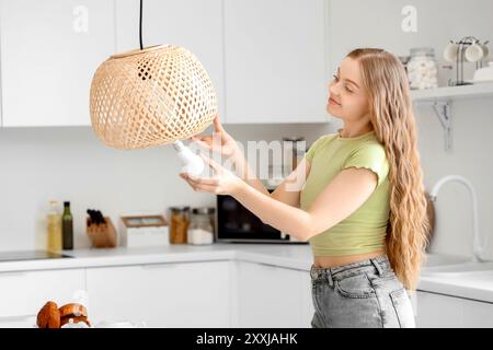 Junge Frau, die Glühbirne in die Lampe in der Küche schraubt Stockfoto