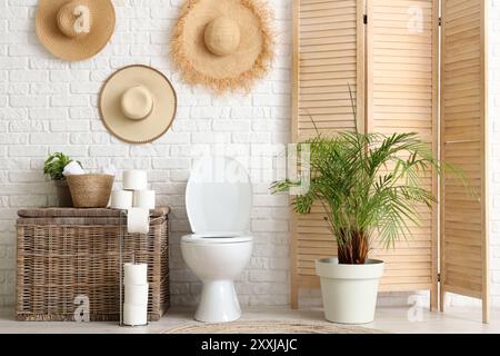 Toilettenschüssel, Wäschekorb und Klappschirm in der Nähe der weißen Ziegelwand im WC Stockfoto