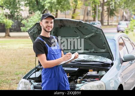 Männlicher Mechaniker schreibt in der Zwischenablage in der Nähe von Autos draußen Stockfoto