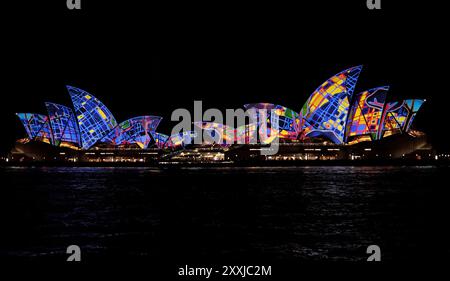 Songlines (2016), ein zusammengesetztes Bild des Sydney Opera House, beleuchtet während des Vivid Sydney Festivals, als zwei Segelschiffe in der Nacht vorbeifahren Stockfoto