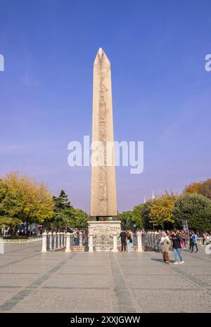 Der Obelisk von Theodosius, ein altägyptisches Denkmal, steht hoch auf dem Istanbuler Sultanahmet-Platz, umgeben von Touristen unter einem klaren blauen Himmel Stockfoto